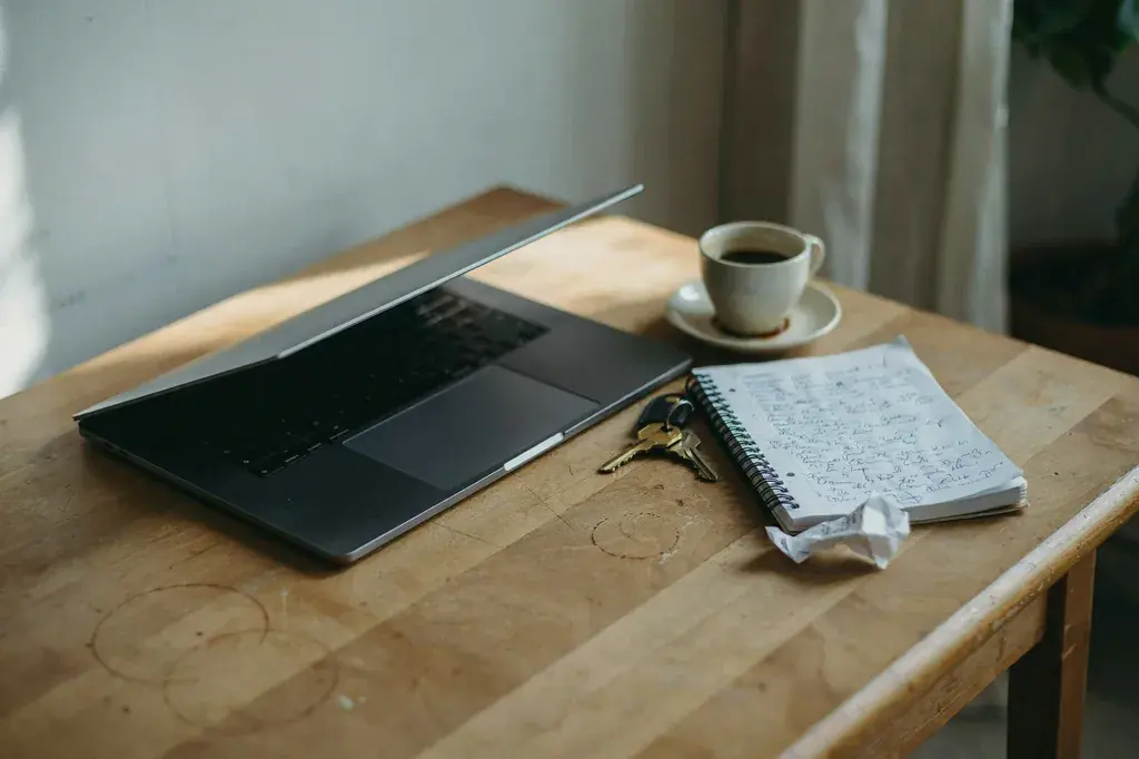 Un escritorio con un notebook abierto, una libreta y una taza de café